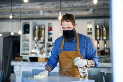 employee in restaurant wiping down tables wearing a mask