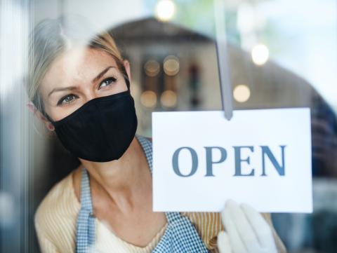 woman wearing mask changing store sign to open